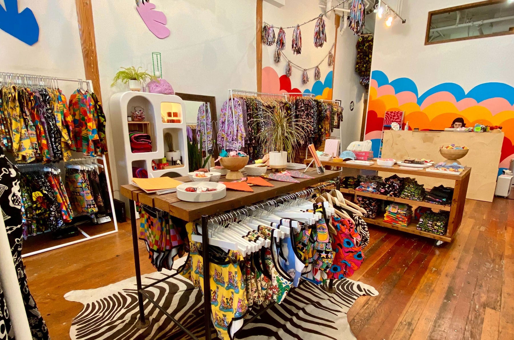 A colorful store with a mural and racks of colorful clothing