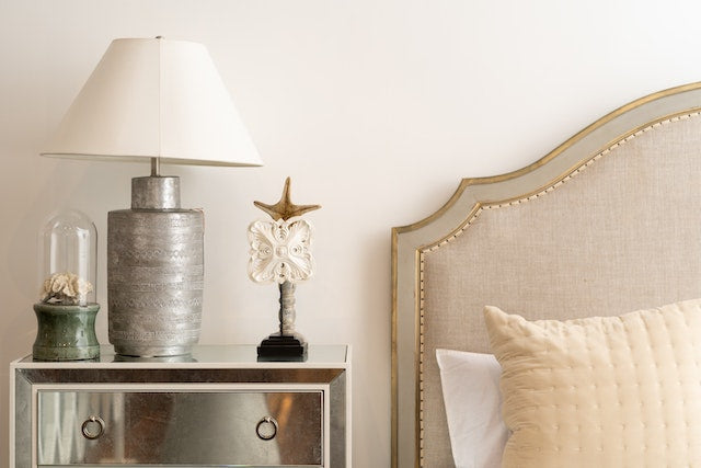 A white lamp on a silver bedside table Caption: Don’t rely just on the overhead lighting.