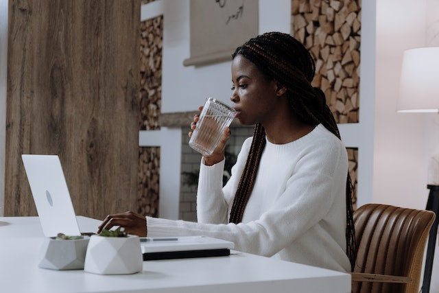 A woman in white drinking water by a laptop. Caption: Biggest home staging mistakes: making it hard for buyers to understand the potential of the rooms by leaving them empty.