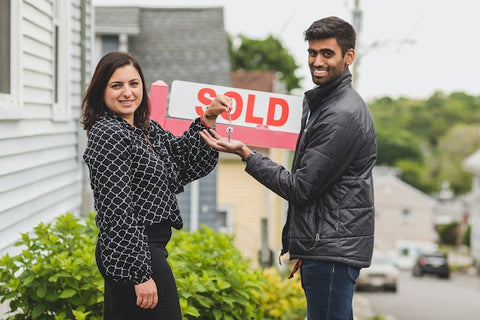 Even after selling your home, nurturing a minimalist mindset can pave the way for a decluttered, intentional lifestyle in your new home. Real estate agent handling the keys to a home to their client while standing next to a sold sign