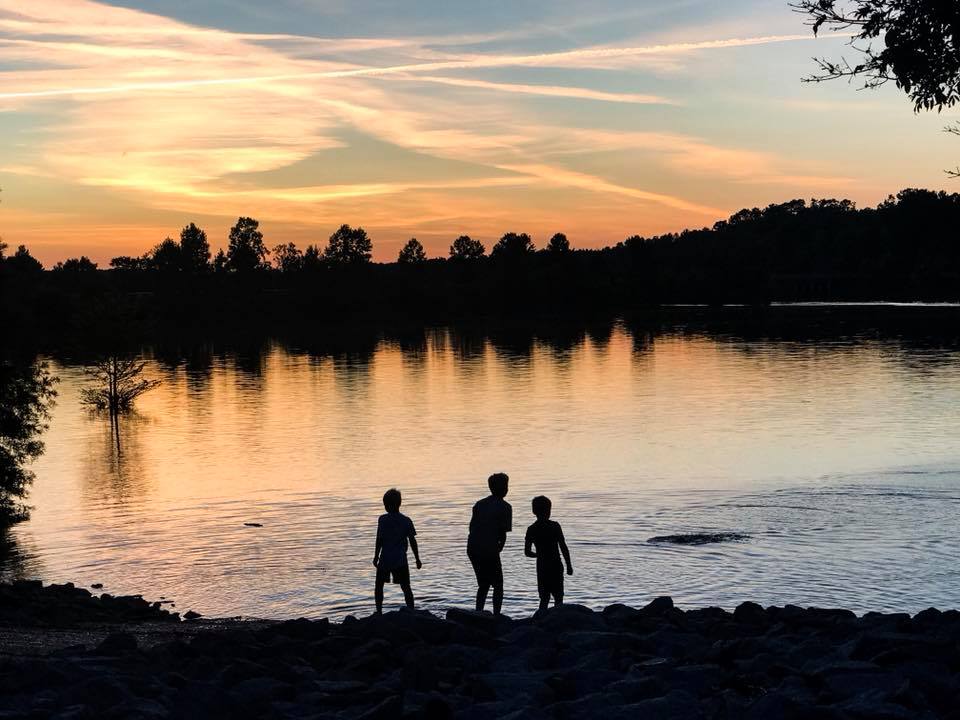 Night photo silhouette of boys skipping rocks on lake