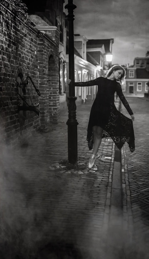 Night photo of woman holding onto a lamp post