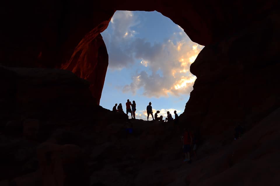 silhouette of people standing outside of a cave