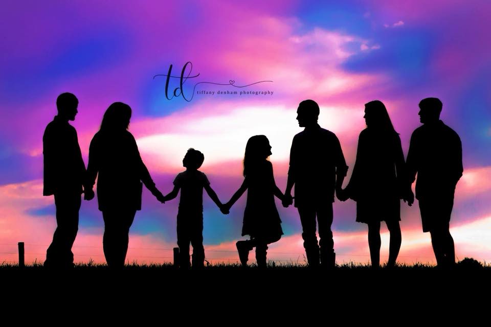 silhouette photograph of family holding hands in front of multicolored sky