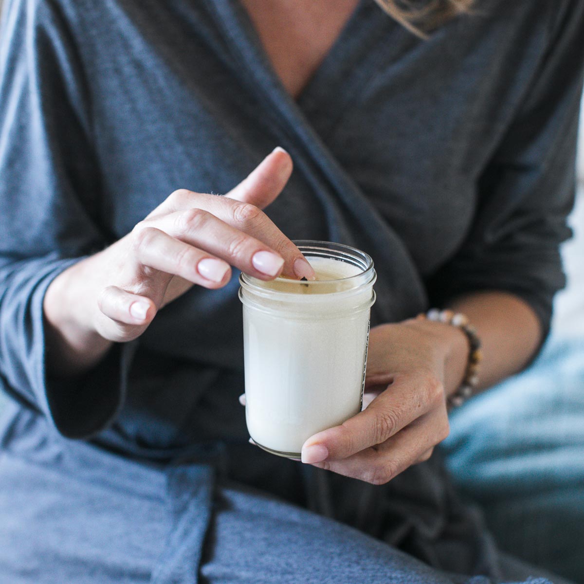 Woman in robe dips her finger into a Soy Lotion Candle jar