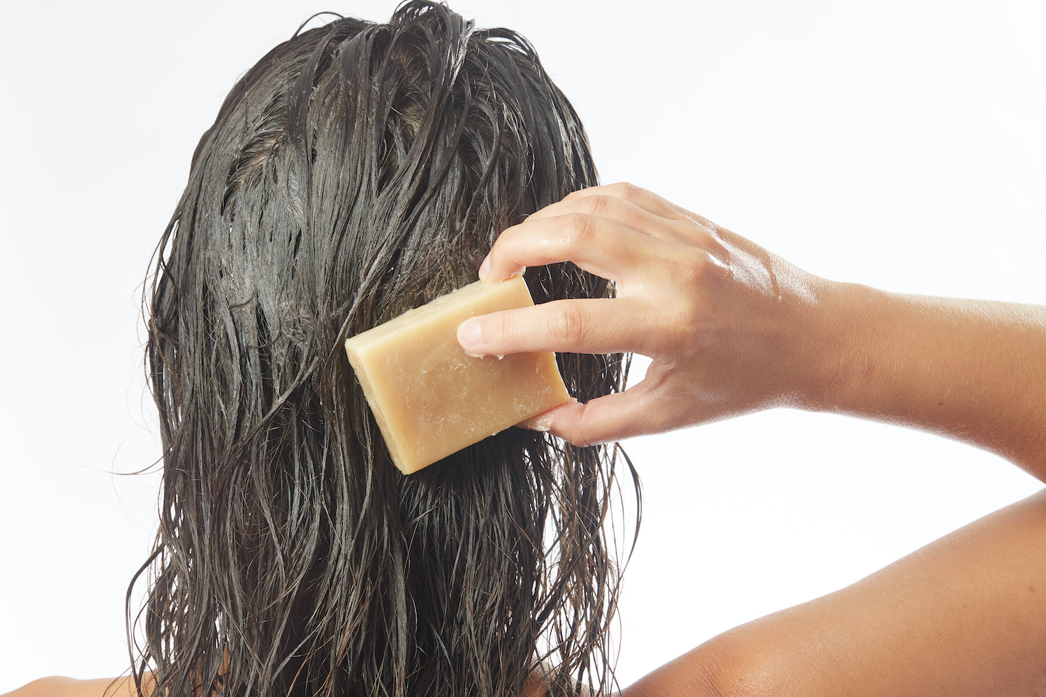 woman rubbing a bar of shampoo on her wet brown hair