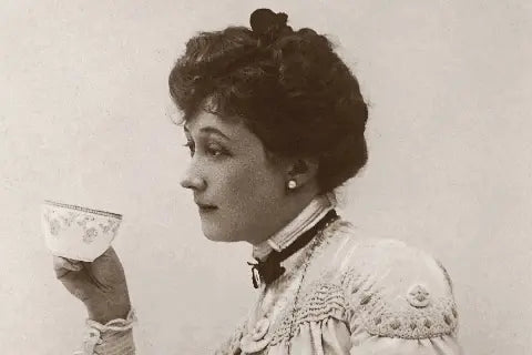 A black and white photograph depicting a Victorian lady drinking tea from a cup