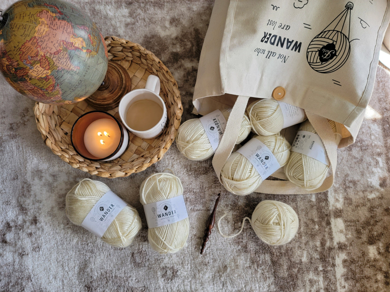 Wander yarn is falling out of a tote bag and onto a rug. A tray holding a globe, coffee, and a candle sit beside it.