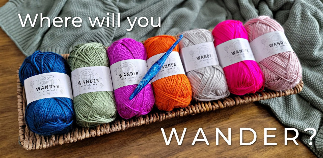 Where will you wander? 7 skeins of Wander acrylic yarn lay on a basket. A bright blue resin crochet hook lays on top.