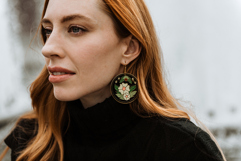 A woman with long red hair in a black turtleneck sweater wears black enamel earrings