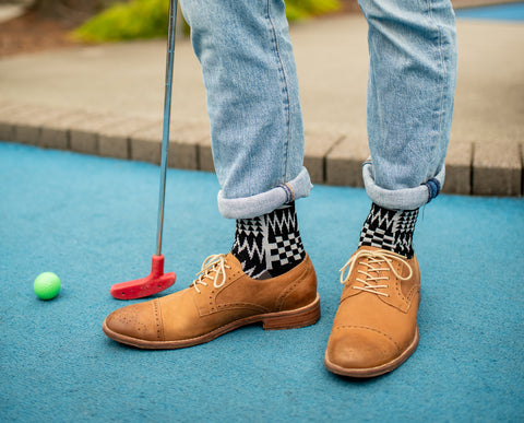 Coast Salish Crew Socks in black and white peek out between brown oxfords and rolled bluejeans