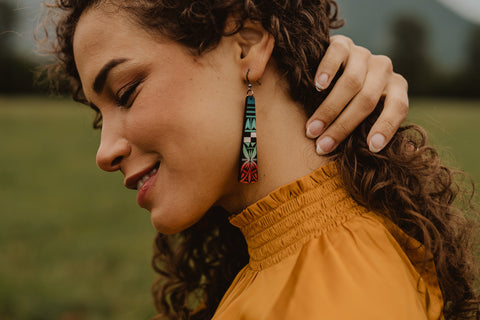A woman in a yellow turtleneck pulls back her curly hair to show a multicolored wood earring.