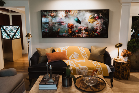 A yellow wool throw blanket on a dark couch under an abstract floral painting