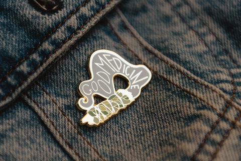 An enamel pin with a stylized bundle of sage; the sage smoke says Good Medicine