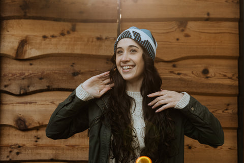 A woman with dark hair models a blue wool beanie in front of a wood slat background