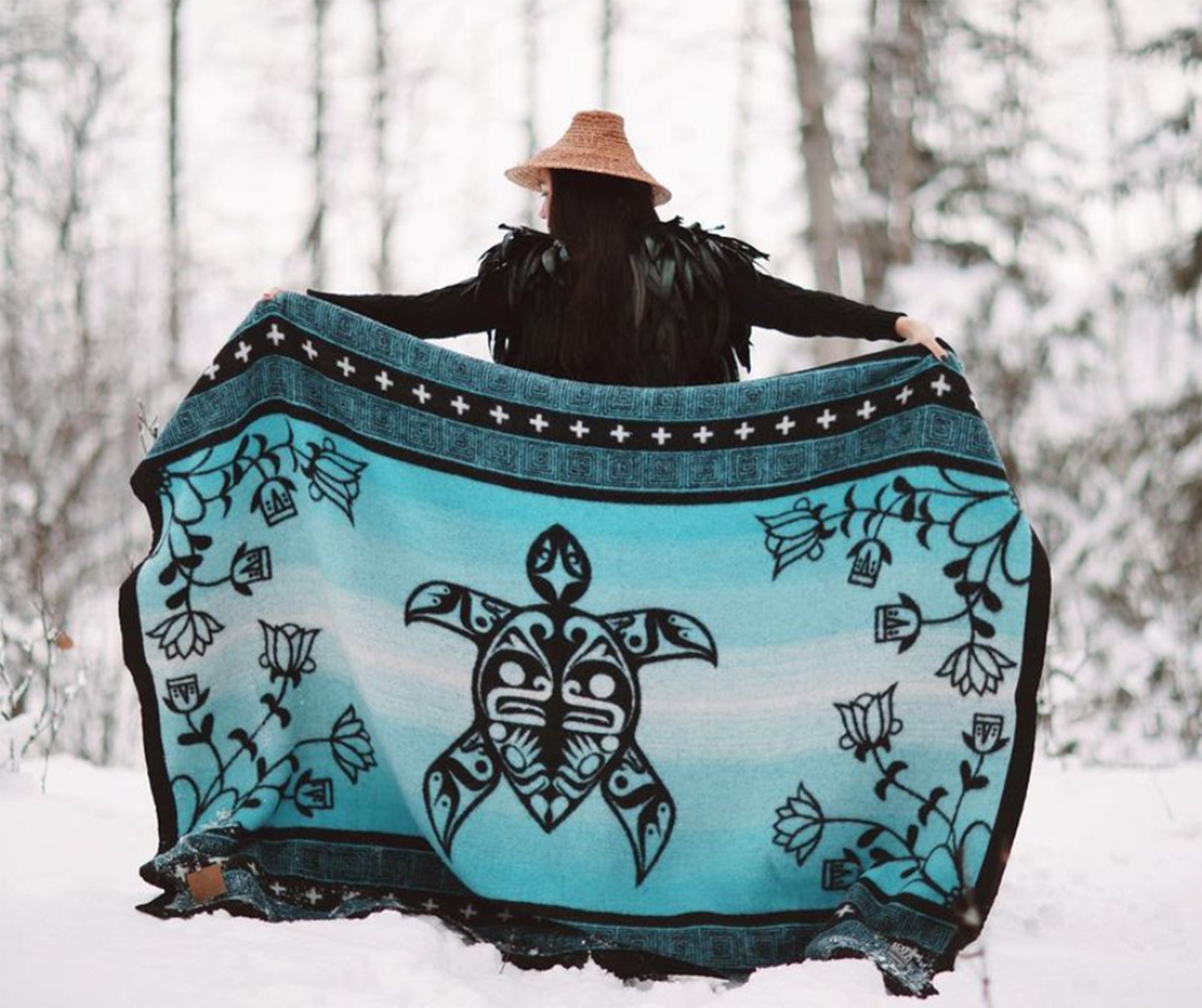 Woman-with-cedar-hat-holds-turquoise-and-black-turtle-design-wool-blanket-stretched-out-behind-her