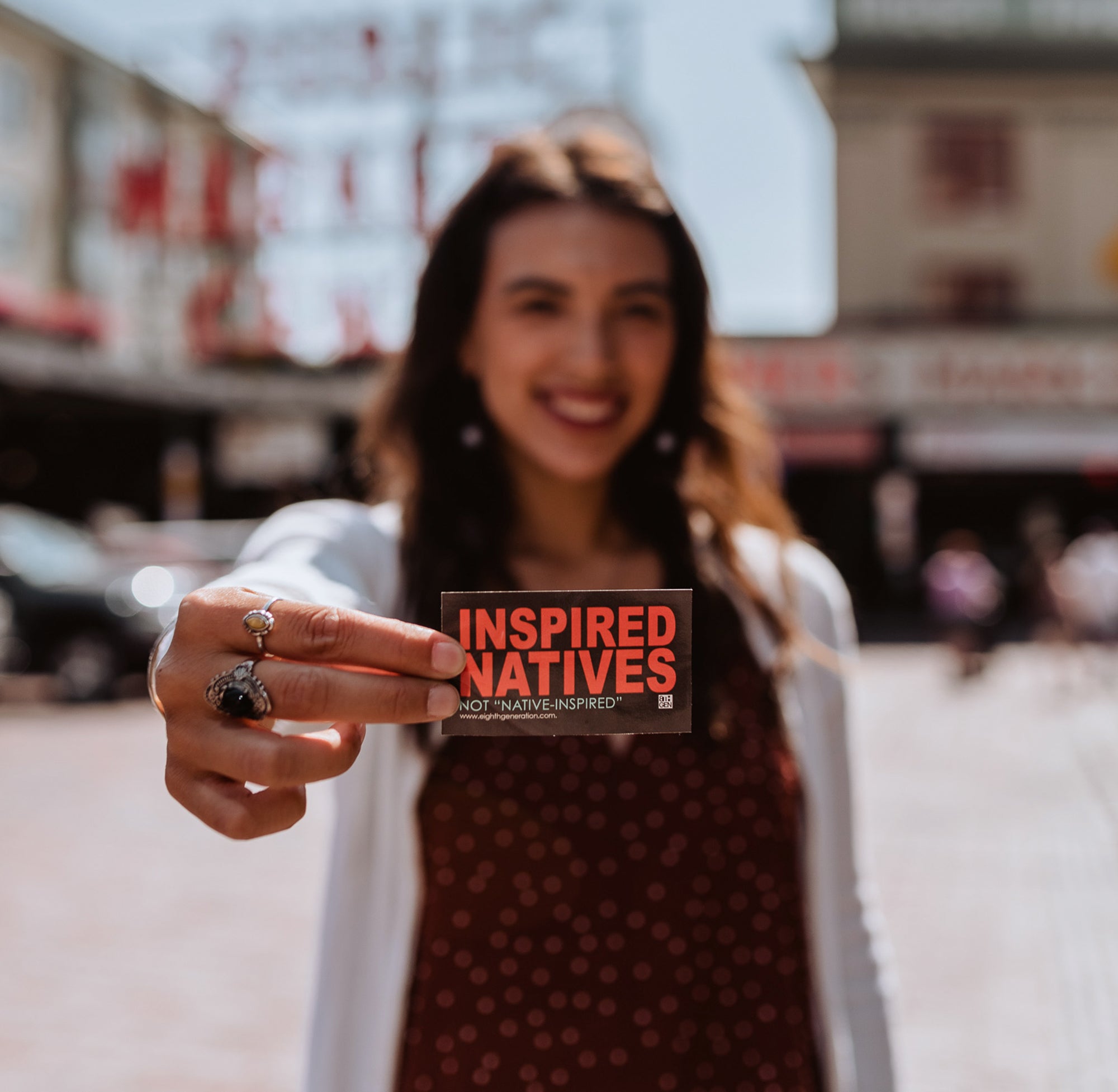 woman-holds-black-sticker-with-red-and-teal-text-that-reads-Inspired-Natives-not-"Native-inspired"-up-to-camera