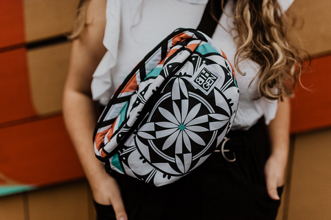A woman in a white shirt wears a hip bag slung across her chest. The bag has an Acoma Pueblo design in black, white, coral, and turquoise.