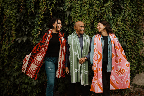 Giani, Robert, and Fran model colorful wool scarves in front of an ivy-covered wall
