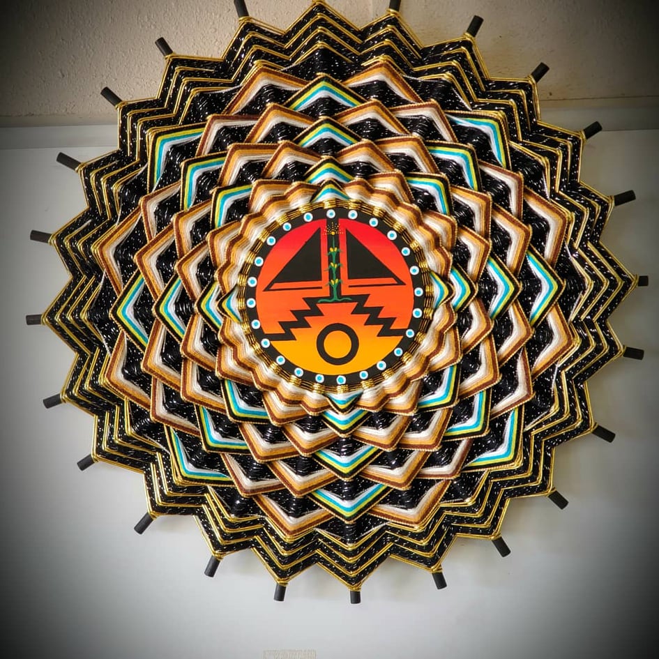 Mandala-featuring-orange-and-black-Navajo-design-in-center-circle-surrounded-by-green-blue-yellow-brown-black-triangle-shaped-weavings
