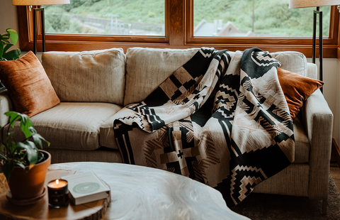 A brown and black wool blanket called "New Phase Throw Blanket" is on a tan couch