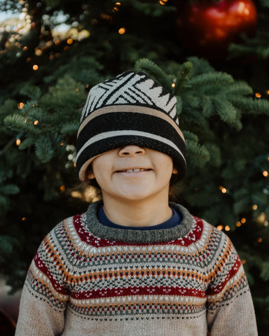 A young Native boy models a tan, black, and white wool beanie in front of a Christmas tree