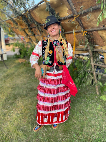 A smiling woman, Sarah Agaton Howes, looks at the camera while wearing her jingle dress regalia