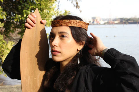 A Tlingit woman in a black coat with a cedar woven headband models earrings in the shape of silver paddles.