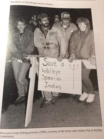 A black and white photo of protesters in 1989. They are protesting the rights guaranteed to Anishinaabe people to practice their traditional ways of fishing and harvesting. 