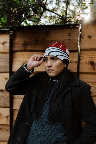 Cassius Johnson, a Diné/Navajo man, models a black, red, and white wool beanie made from a Native American-designed blanket
