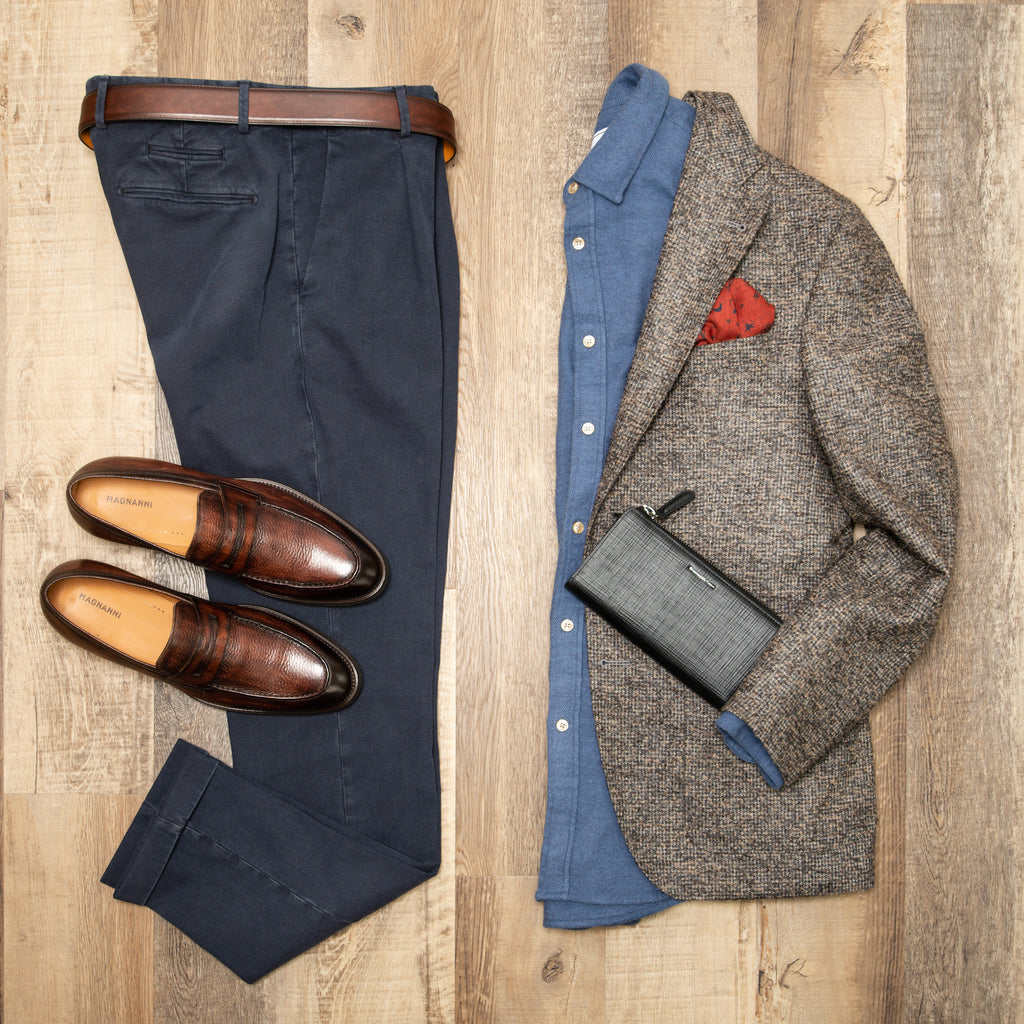 Flat lay photo of navy trousers, brown loafers, light blue portuguese flannel shirt, textured brown sport jacket, and black zegna wallet