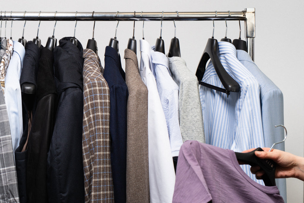 Clothing on hangers on a metal rack, with a hand pulling one item off the rack