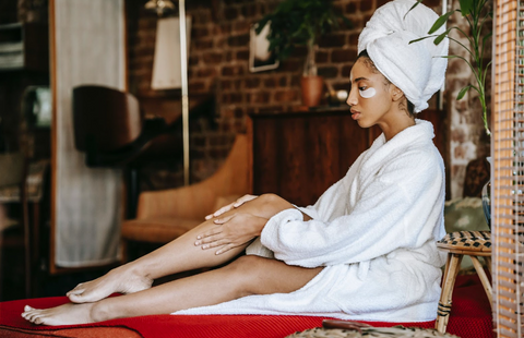 A woman in a bathrobe applying cream on her leg