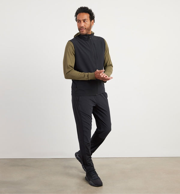 Male model sports the new Oslo Travel Vest worn with black athletic pants and a long sleeve t-shirt hoodie.