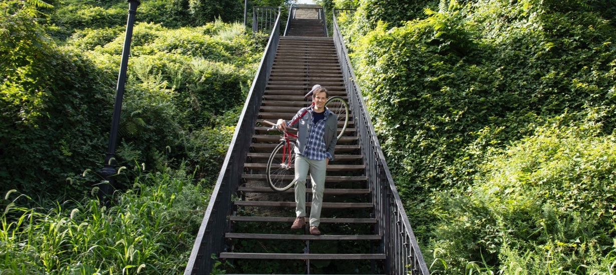 Stefan carries his bike down steps lined with greenery.