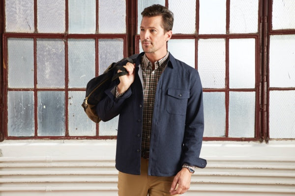 Our Gramercy Shirt Jacket in Blue Hour layered over a dress shirt, with a bag slung over the model's shoulder.