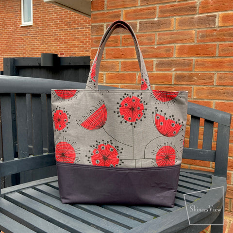 A market tote bag that is gray with red flowers sitting on a gray bench in front of a red-brick wall.