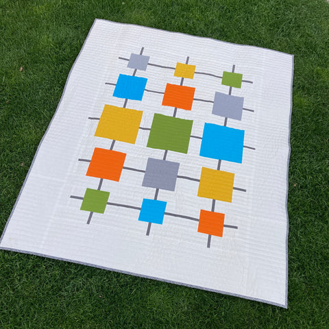 White quilt with colorful squares for a mid-century modern style lying on the grass