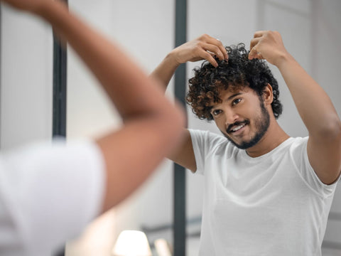 A confident man with curly hair, demonstrating proper hair care practices. Adopting a diligent hair care routine can play a crucial role in preventing hair loss and promote healthy hair growth.