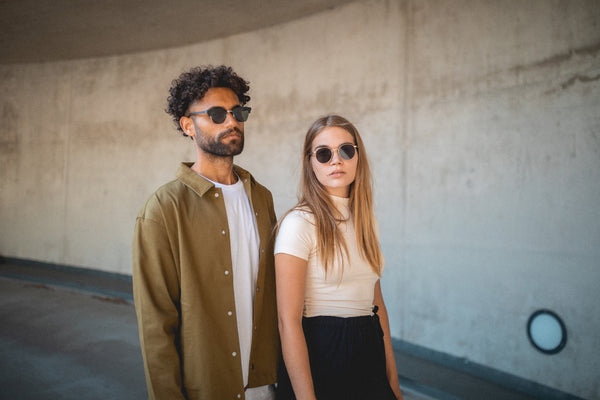 Lynch nachhaltige Sonnenbrille aus Holz mit Metall und schwarzem TR90 mit schwarzen Eichenholzbügeln und Janis nachhaltige Metallsonnenbrille mit rosegoldenen Rahmen und graue Sonnenbrillengläser mit 100% UV Schutz und UV400Filter und Rückentspiegelung von TAKE A SHOT aus Leipzig Paarbild im Parkhaus Zoo Leipzig