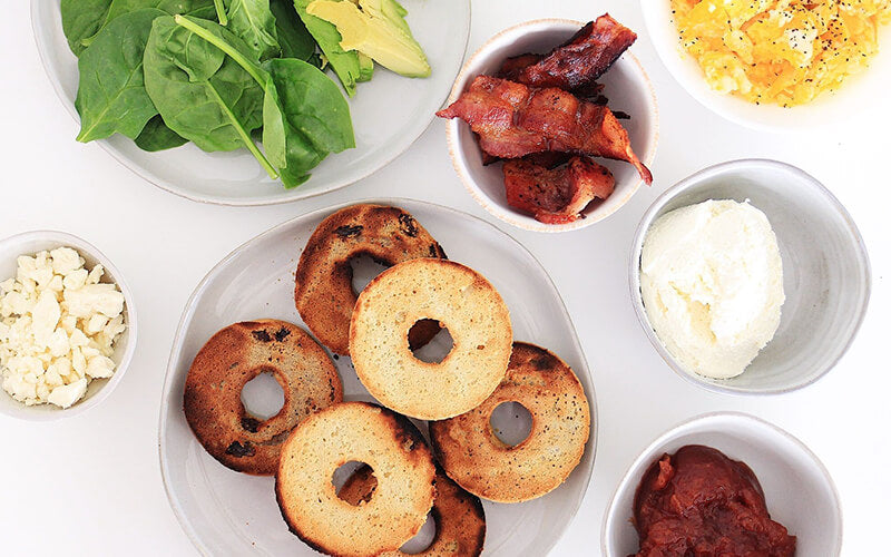 PBH Foods Keto Bagels with dishes of bacon, cheese, eggs, spinach