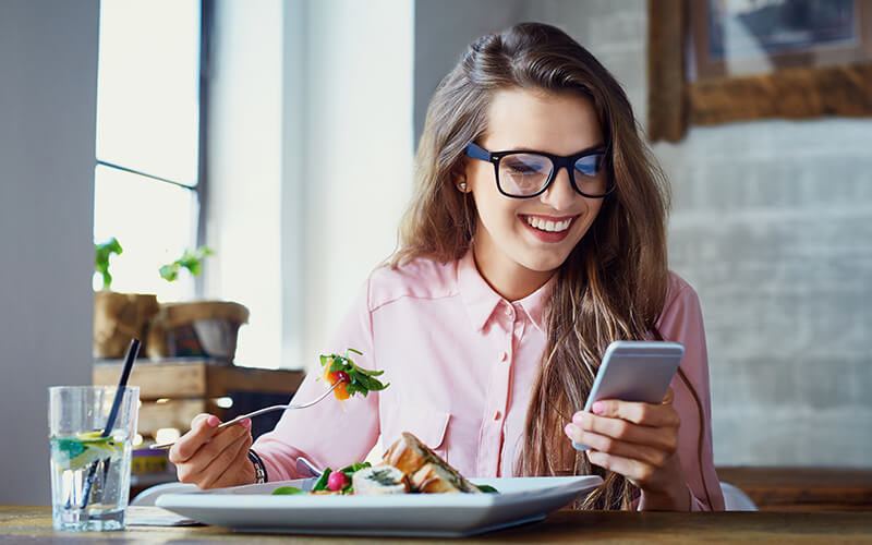 Female eating at table while looking at her phone