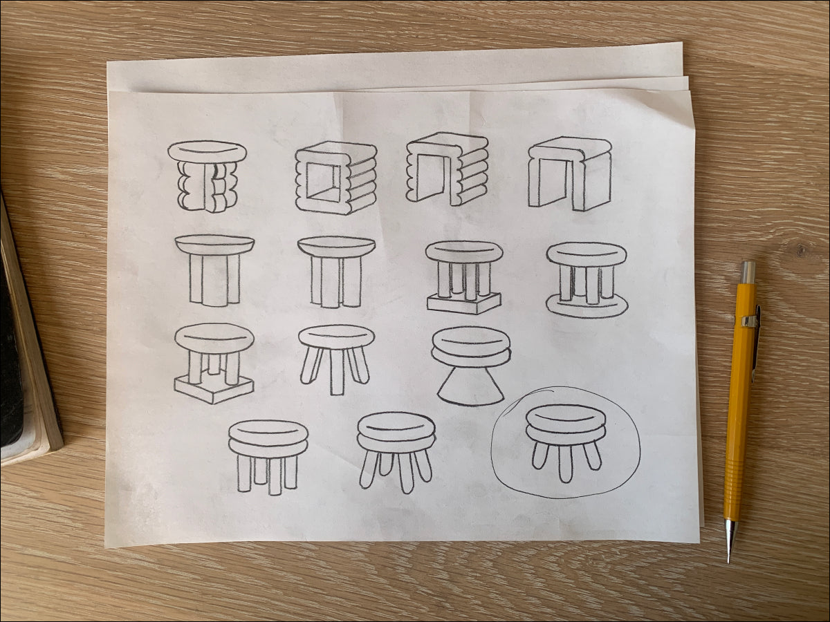 A sketch of several different stool designs sitting on a wood tabletop. A yellow pencil sits to the right of the drawings.