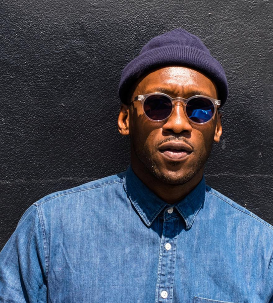 Mahershala Ali wearing a beanie and shades for a photo.