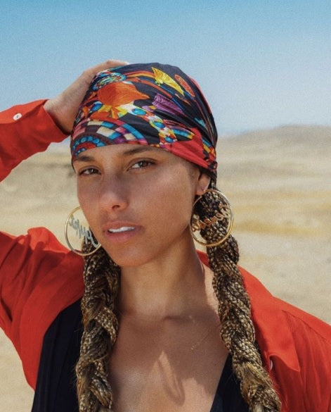 Alicia Keys in braids wearing a red shirt in the dessert.