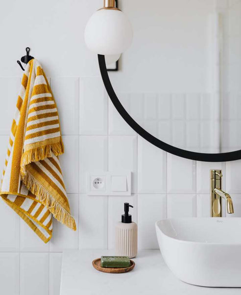 Bathroom sink with a round mirror and yellow towel.