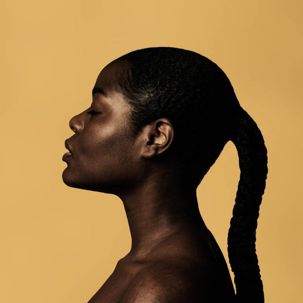 Girl in a braided ponytail posing sideways against a yellow background.