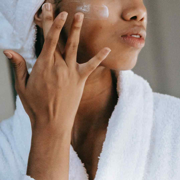 Black girl applying moisturizer on her face.