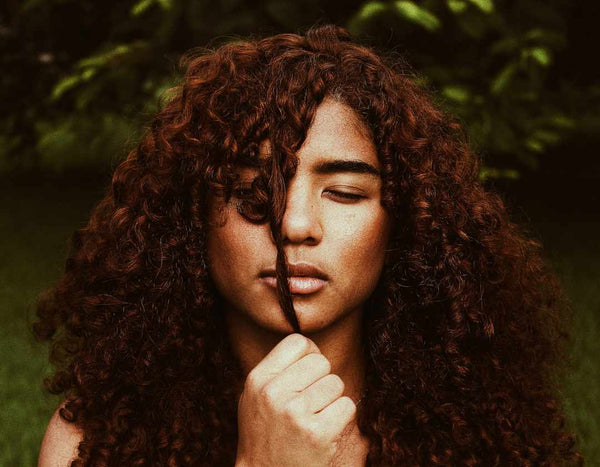 Black girl holding her curly bangs in front of her face.