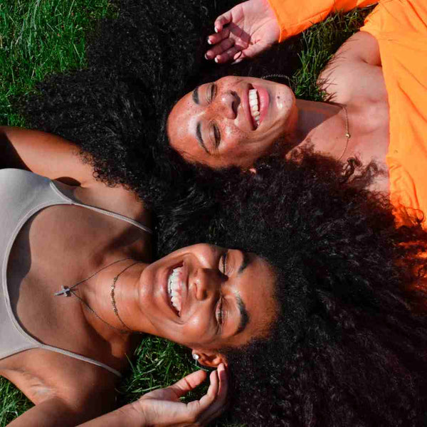 Two girls with curly hair laying on grass.